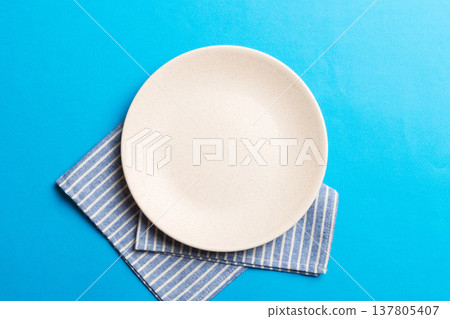 Top view on colored background empty round white plate on tablecloth for food. Empty dish on napkin with space for your design Top view on colored background empty round white plate on tablecloth for food. Empty dish on napkin with space for your design 137805407