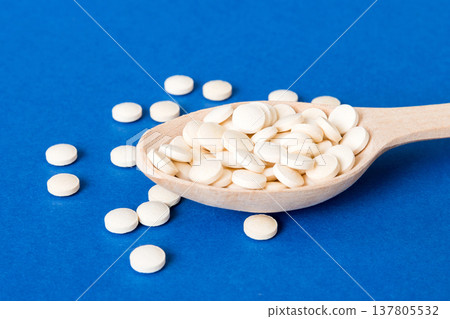 Heap of white pills on colored background. Tablets scattered on a table. Pile of red soft gelatin capsule. Vitamins and dietary supplements concept Heap of white pills on colored background. Tablets scattered on a table. Pile of red soft gelatin capsule. Vitamins and dietary supplements concept 137805532