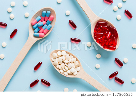 Vitamin capsules in a spoon on a colored background. Pills served as a healthy meal. Red soft gel vitamin supplement capsules on spoon 137805535