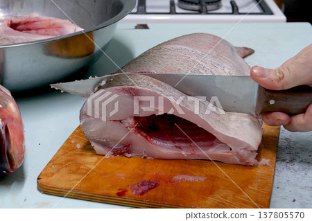 Man prepares fresh silver carp fish. Cuts it into steaks with a knife. home cooking concept Man prepares fresh silver carp fish. Cuts it into steaks with a knife. home cooking concept 137805570
