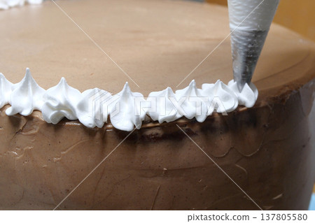 A woman pastry chef with a pastry bag in her hands squeezes cream on a cake in a home kitchen. Professional chef at work on bakery kitchen. culinary, baking and cooking food concept, home cooking A woman pastry chef with a pastry bag in her hands squeezes cream on a cake in a home kitchen. Professional chef at work on bakery kitchen. culinary, baking and cooking food concept, home cooking 137805580