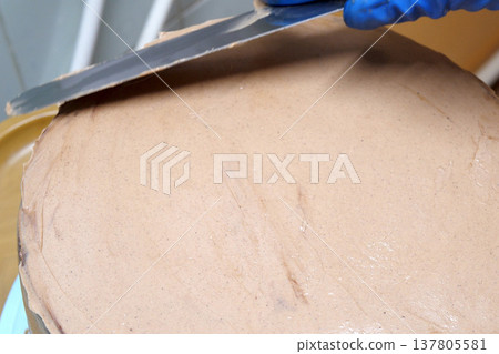 Confectioner woman is smearing cream on sides of cake using spatula, closeup view. culinary, baking and cooking food concept, home cooking Confectioner woman is smearing cream on sides of cake using spatula, closeup view. culinary, baking and cooking food concept, home cooking 137805581