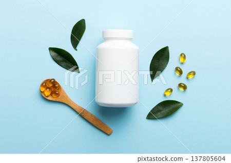 Omega-3 capsules lie in white bottle on a table with green leaves background. Fish oil tablets. Biologically active additives. omega 6, omega 9, vitamin A, E, D, vitamin D3 top view with copy space Omega-3 capsules lie in white bottle on a table with green leaves background. Fish oil tablets. Biologically active additives. omega 6, omega 9, vitamin A, E, D, vitamin D3 top view with copy space 137805604