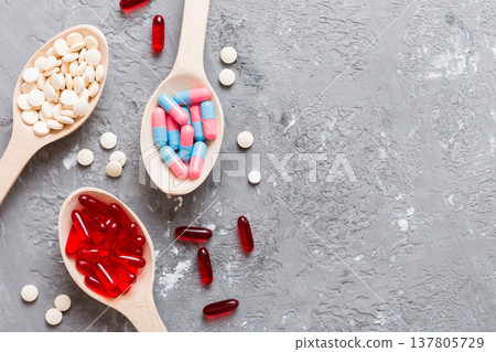 Vitamin capsules in a spoon on a colored background. Pills served as a healthy meal. Red soft gel vitamin supplement capsules on spoon 137805729
