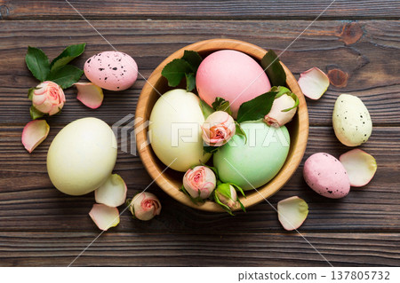 Happy Easter. Easter eggs in basket on colored table with yellow roses. Natural dyed colorful eggs background top view with copy space Happy Easter. Easter eggs in basket on colored table with yellow roses. Natural dyed colorful eggs background top view with copy space 137805732