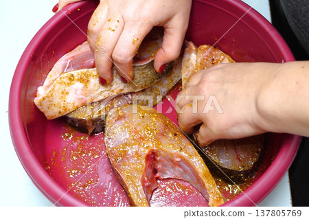 Marinated fish with spices. Before cooking, the hand of the cook smears butter and spices. home cooking concept Marinated fish with spices. Before cooking, the hand of the cook smears butter and spices. home cooking concept 137805769