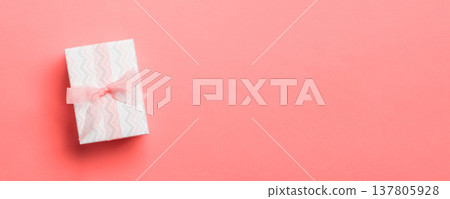 wrapped Christmas or other holiday handmade present in paper with pink ribbon on living coral background. Present box, decoration of gift on colored table, top view with copy space wrapped Christmas or other holiday handmade present in paper with pink ribbon on living coral background. Present box, decoration of gift on colored table, top view with copy space 137805928