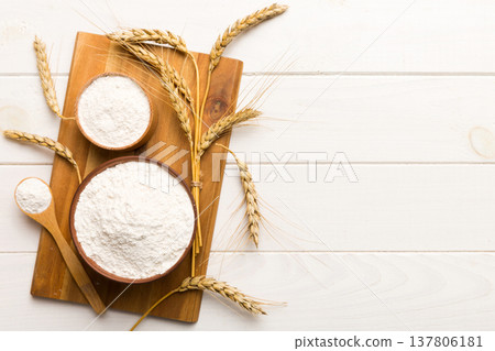 Flat lay of Wheat flour in wooden bowl with wheat spikelets on colored background. world wheat crisis Flat lay of Wheat flour in wooden bowl with wheat spikelets on colored background. world wheat crisis 137806181