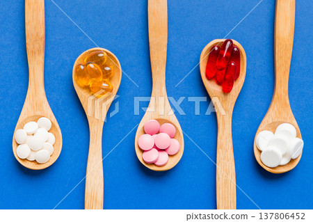 Vitamin capsules in a spoon on a colored background. Pills served as a healthy meal. Red soft gel vitamin supplement capsules on spoon 137806452