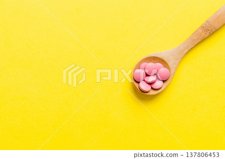 Vitamin capsules in a spoon on a colored background. Pills served as a healthy meal. Red soft gel vitamin supplement capsules on spoon 137806453