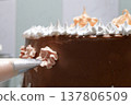 A woman pastry chef with a pastry bag in her hands squeezes cream on a cake in a home kitchen. Professional chef at work on bakery kitchen. culinary, baking and cooking food concept, home cooking 137806509