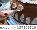 A woman pastry chef with a pastry bag in her hands squeezes cream on a cake in a home kitchen. Professional chef at work on bakery kitchen. culinary, baking and cooking food concept, home cooking 137806510