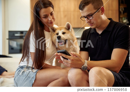 Guy is holding smartphone. Man and woman are sitting at home with Shibu Inu dog Guy is holding smartphone. Man and woman are sitting at home with Shibu Inu dog 137806958