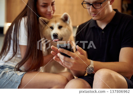 Guy is holding smartphone. Man and woman are sitting at home with Shibu Inu dog Guy is holding smartphone. Man and woman are sitting at home with Shibu Inu dog 137806962