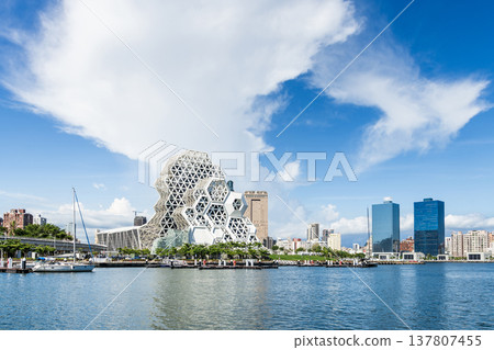 Panoramic view of the Kaohsiung Music Center and buildings along the harbor waterfront. The white hexagonal building structure on the shore of Love Pier. 137807455