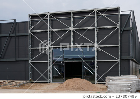 Modern Industrial Building Under Construction with Steel Frame Facade and Large Glass Entrance Modern Industrial Building Under Construction with Steel Frame Facade and Large Glass Entrance 137807499