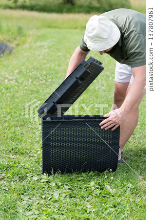 Man assembling outdoor storage container in a grassy area. Easy setup for garden organization. Man assembling outdoor storage container in a grassy area. Easy setup for garden organization. 137807961