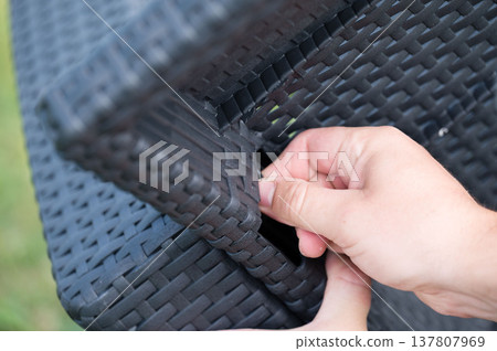 Close-up of a hand assembling dark woven plastic furniture. 137807969
