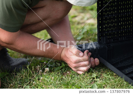 Person assembling outdoor furniture on grass. Hands connect wicker-style pieces. Person assembling outdoor furniture on grass. Hands connect wicker-style pieces. 137807976