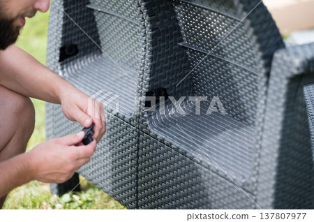 Man assembling outdoor wicker furniture. Easy-to-use connectors for quick setup. Man assembling outdoor wicker furniture. Easy-to-use connectors for quick setup. 137807977