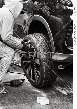 Person works on changing a tire of a car in a garage during the day 137807993