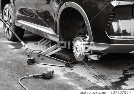 Car repair takes place at an auto shop with a jack lifting a vehicle for tire maintenance and inspection in the afternoon 137807994