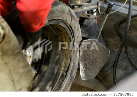 Removing a tire from a car rim. Mechanic works on changing a tire on a vehicle in a workshop during the day Removing a tire from a car rim. Mechanic works on changing a tire on a vehicle in a workshop during the day 137807995