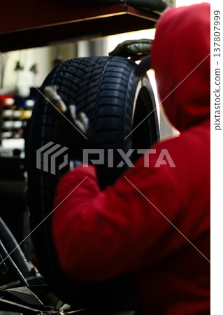 Tire repair workshop with a worker applying sealant to a tire during the day 137807999