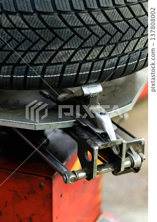 Tire changing equipment in a workshop showing the process of mounting a tire on a rim 137808002