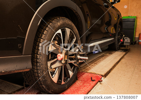 Car wheel alignment process taking place in a garage during daylight hours. Wheel alignment and alignment on the car service platform. 137808007