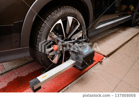 Wheel alignment and alignment on the car service platform. Worker uses equipment to check wheel alignment in auto repair shop during afternoon 137808008