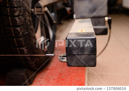 Wheel alignment and alignment on the car service platform. Close view of a car part with a wire near a tire during a mechanical inspection in a garage at midday Wheel alignment and alignment on the car service platform. Close view of a car part with a wire near a tire during a mechanical inspection in a garage at midday 137808010