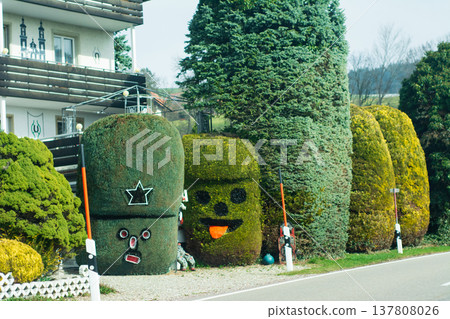 Whimsical topiary figures bring charm to a roadside garden in springtime, evoking smiles and curiosity from passersby in a serene neighborhood setting 137808026