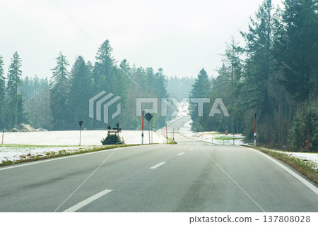 Serene winter road winding through a tranquil forest landscape under a soft cloudy sky during the early morning hours Serene winter road winding through a tranquil forest landscape under a soft cloudy sky during the early morning hours 137808028