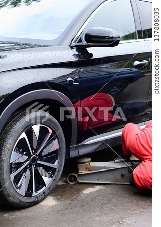 Mechanic works on a black SUV using a jack to lift the vehicle in a garage 137808035