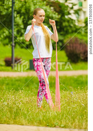 Girl doing exercises outdoor, using resistance fit band. 137808098