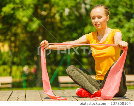 Girl doing exercise outdoor, using resistance fit band. 137808104