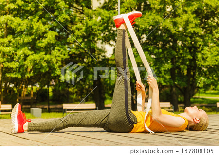 Girl doing exercises outdoor, using fit band. 137808105