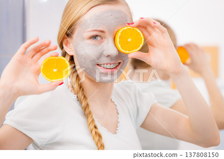 Happy young woman having face mask holding kiwi Happy young woman having face mask holding kiwi 137808150