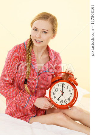 Sleepy woman wearing pajamas holding clock Sleepy woman wearing pajamas holding clock 137808165