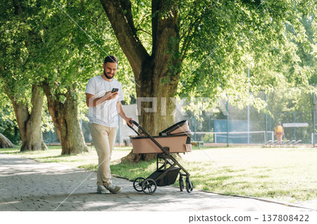 Using smartphone. Father is with cradle, having a walk in the park 137808422