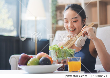 Fit young Asian women in activewear sitting on yoga mat and eating fresh vegetable salad after workout, representing clean eating, fitness lifestyle, wellness routine and health balance. 137808571