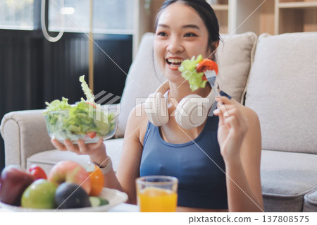 Fit young Asian women in activewear sitting on yoga mat and eating fresh vegetable salad after workout, representing clean eating, fitness lifestyle, wellness routine and health balance. Fit young Asian women in activewear sitting on yoga mat and eating fresh vegetable salad after workout, representing clean eating, fitness lifestyle, wellness routine and health balance. 137808575