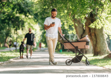 Smartphone in hand. Father is with cradle, having a walk in the park Smartphone in hand. Father is with cradle, having a walk in the park 137808643