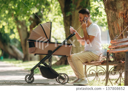 Talking by phone. Father is with cradle, having a walk in the park 137808652