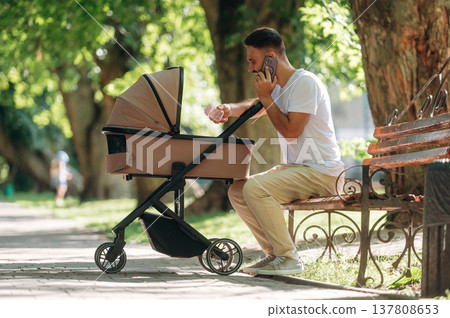 Talking by phone. Father is with cradle, having a walk in the park 137808653