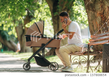 Having a conversation by phone. Father is with cradle, having a walk in the park Having a conversation by phone. Father is with cradle, having a walk in the park 137808654