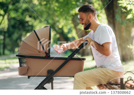 Side view, sitting on the bench. Father is with cradle, having a walk in the park 137808662