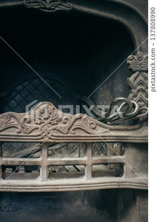 Old iron fireplace with decorative fireguard range and fireplace accessories. Fireplace poker and scoop in vintage metal fireplace. Clean fireplace with soot and forged steel. Firewood grates closeup Old iron fireplace with decorative fireguard range and fireplace accessories. Fireplace poker and scoop in vintage metal fireplace. Clean fireplace with soot and forged steel. Firewood grates closeup 137808990