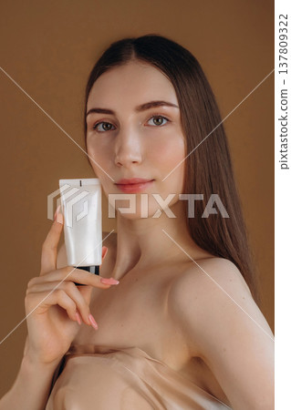 Brand new cream, quality product. Young woman is against background Brand new cream, quality product. Young woman is against background 137809322